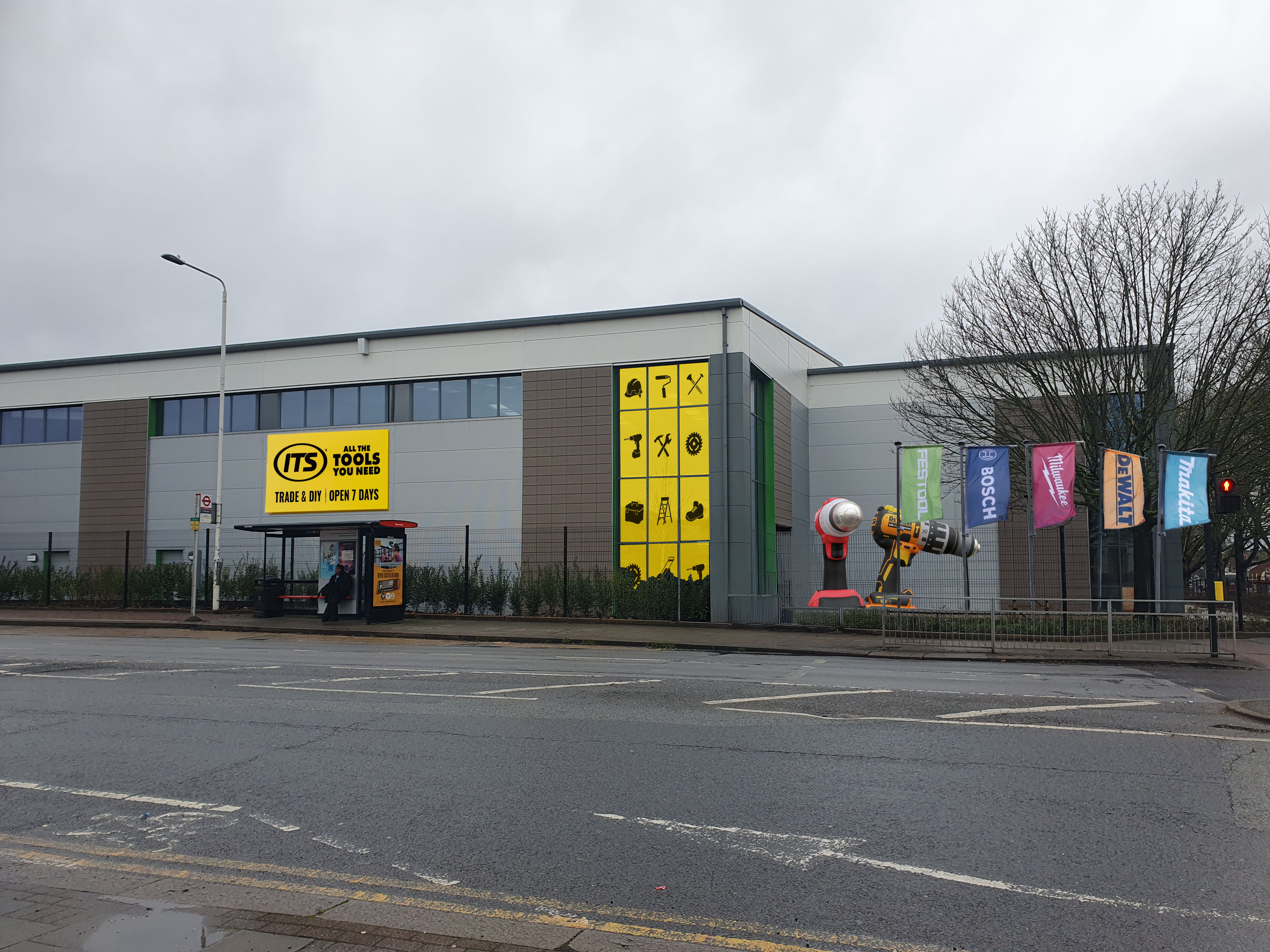 Gray building with large yellow sign and colorful banners on a cloudy day.