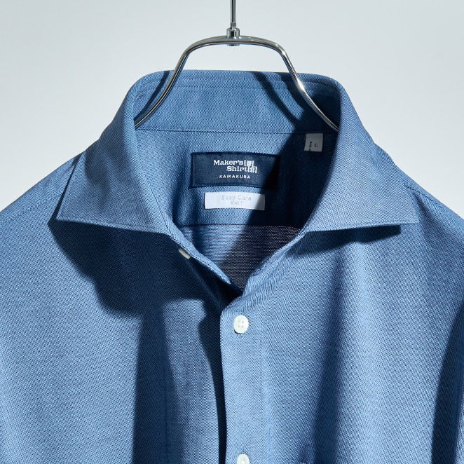 A blue collared shirt hanging on a hanger against a light background.