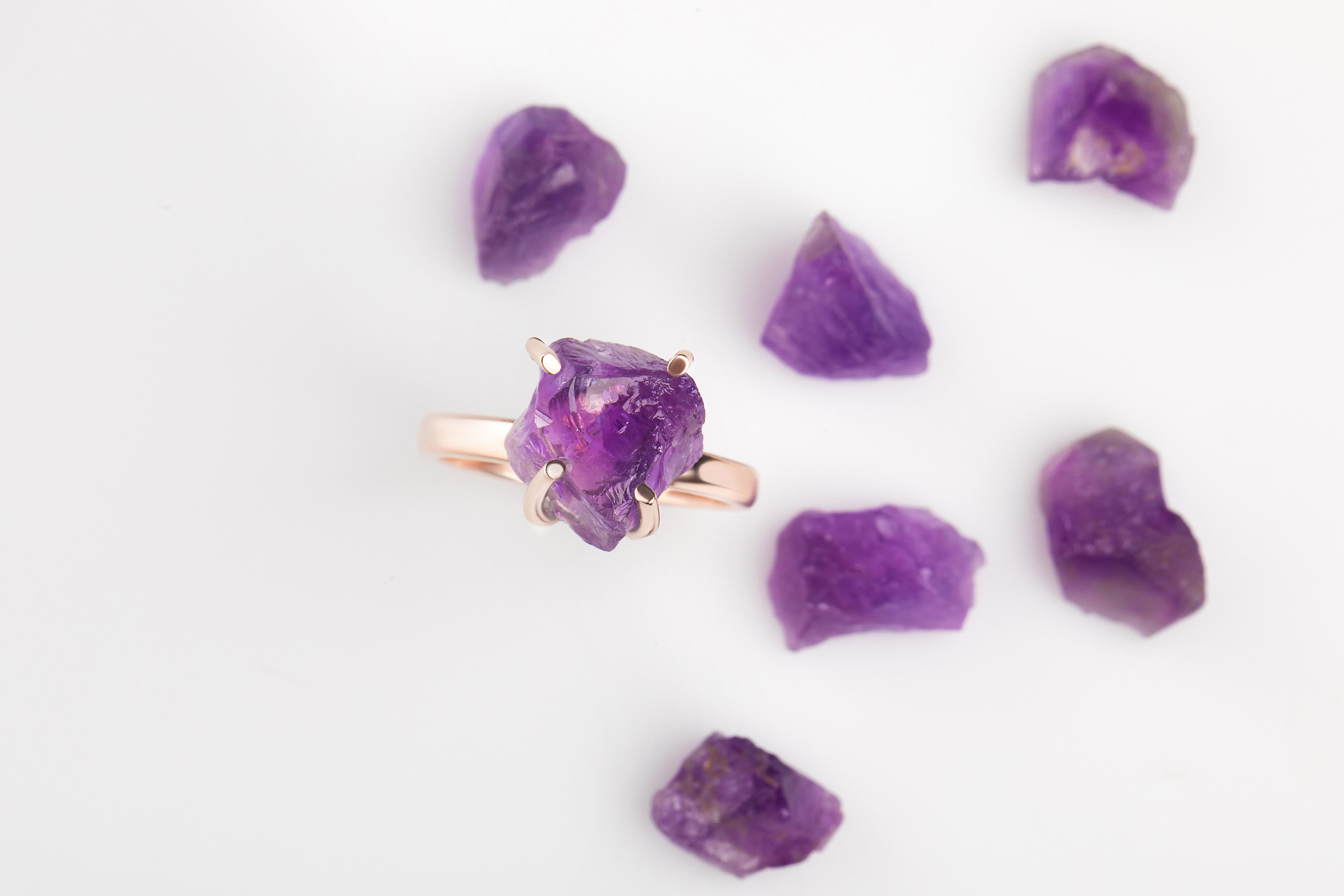 The Raw Crystal Ring - Amethyst is presented next to six raw Amethyst gemstones on a white surface.
