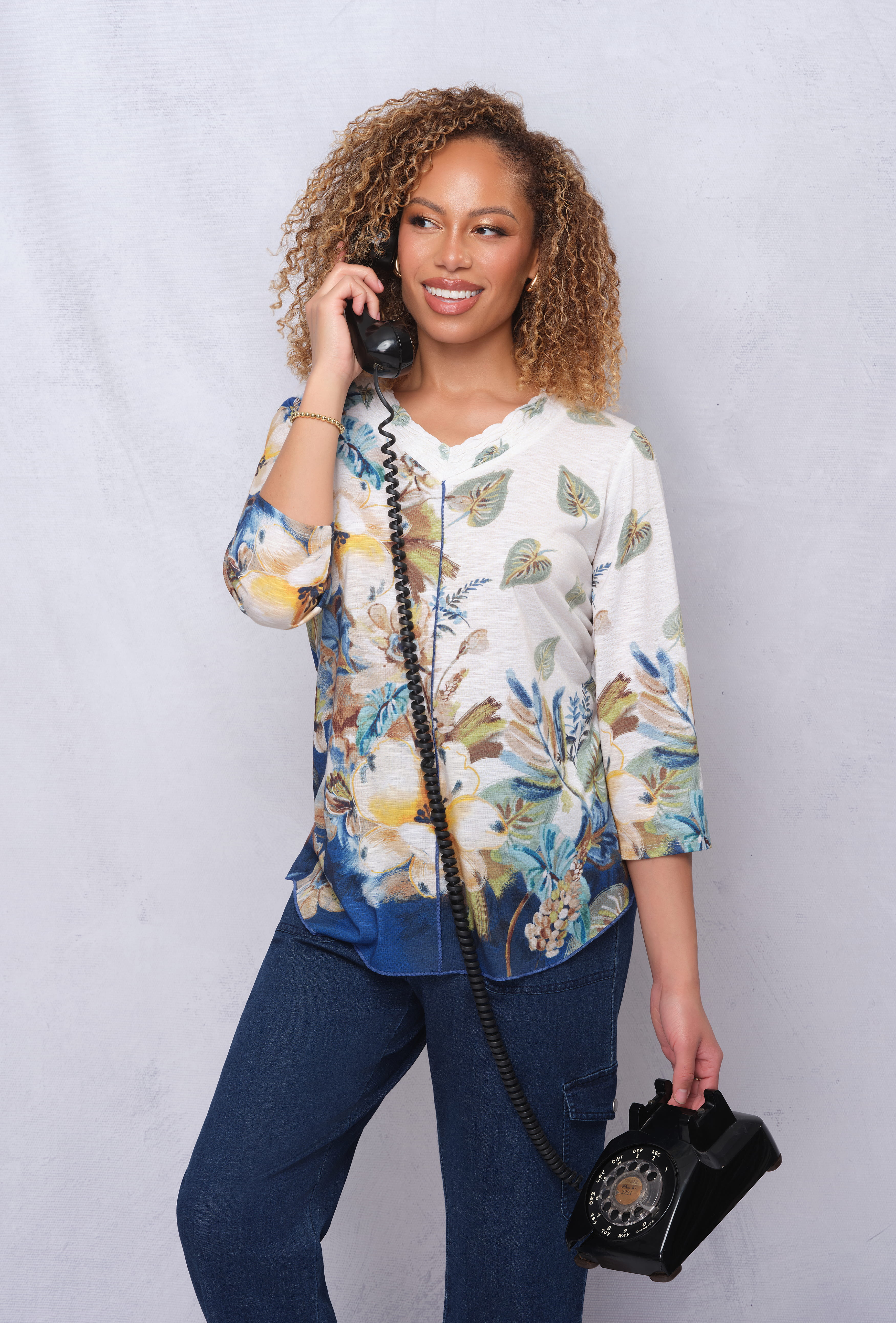 Woman with curly hair talking on a vintage telephone, wearing a floral shirt.