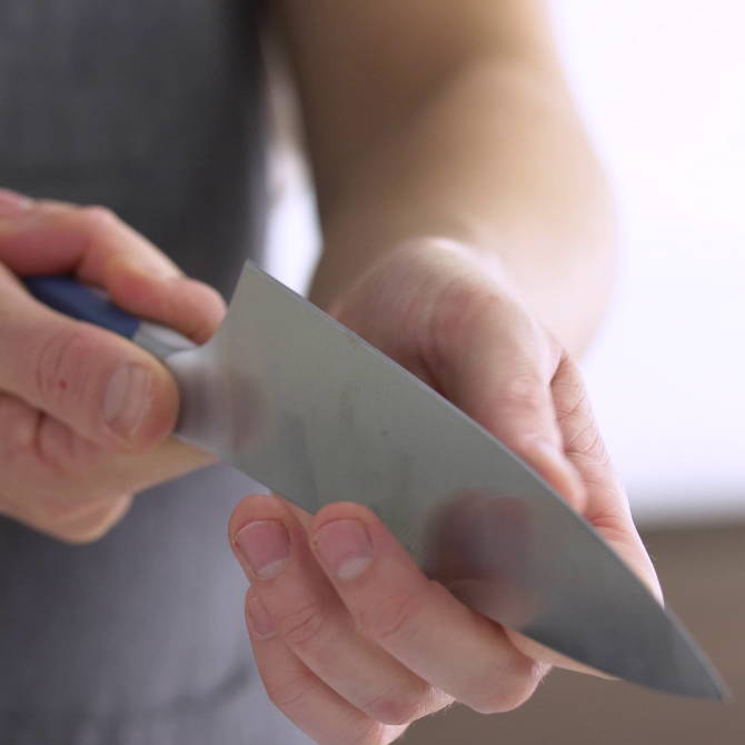 A chef holding a knife blade edge up to inspect for damage along the cutting edge. 
