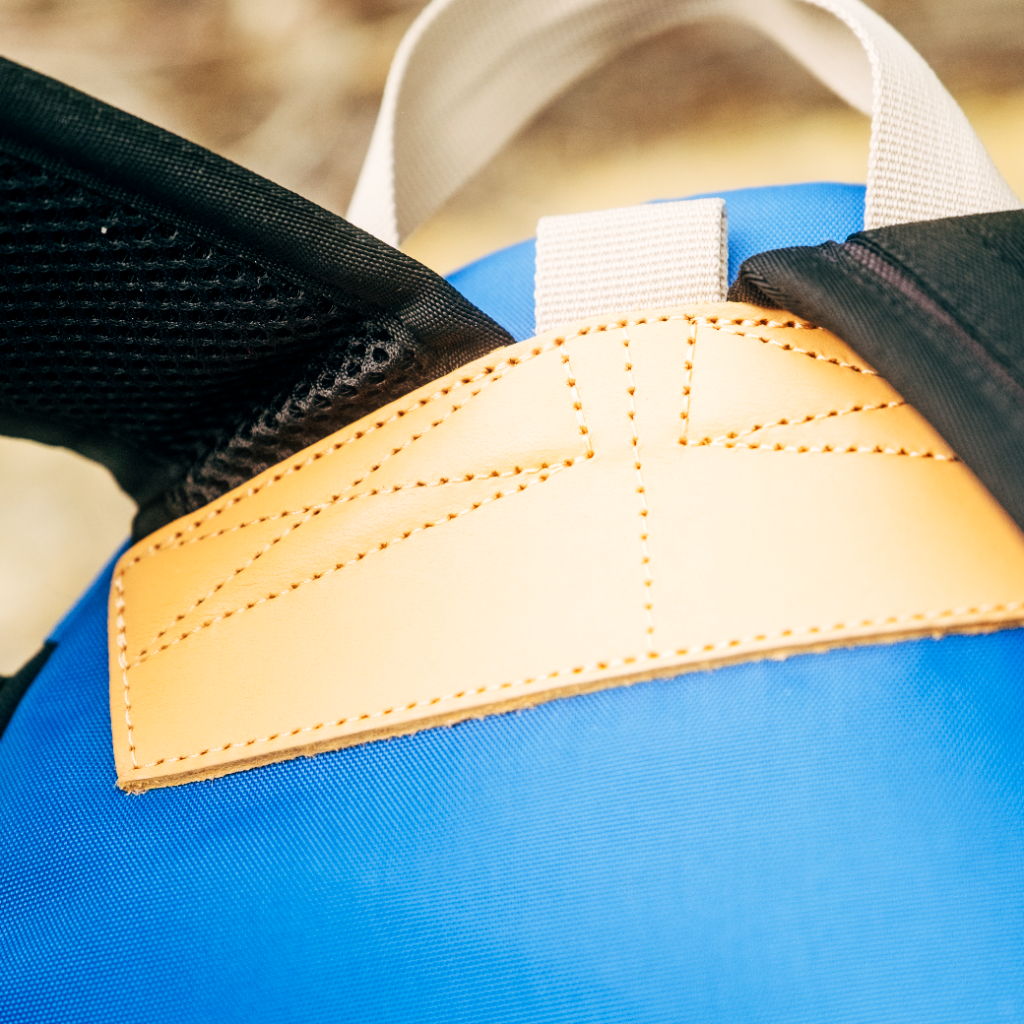 Close-up of a blue backpack strap with a tan leather accent.
