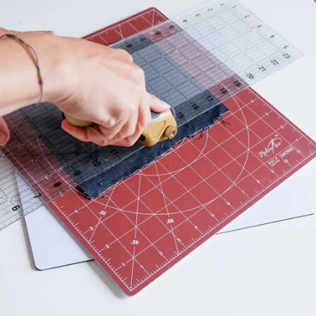 Cutting a piece of denim fabric with a rotary cutter on a rotating cutting mat