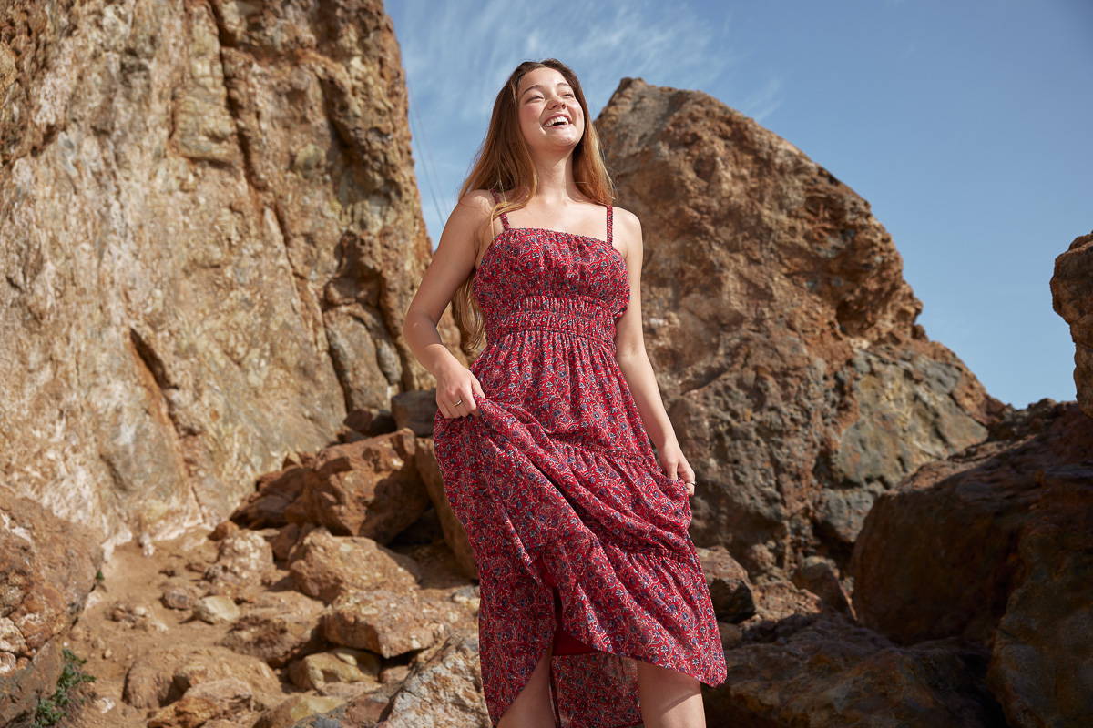 Trixxi sun-kissed summer, girl at oceanside at rocks in red paisley floral maxi sundress.