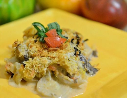 A plate of creamy casserole topped with herbs and diced tomatoes.