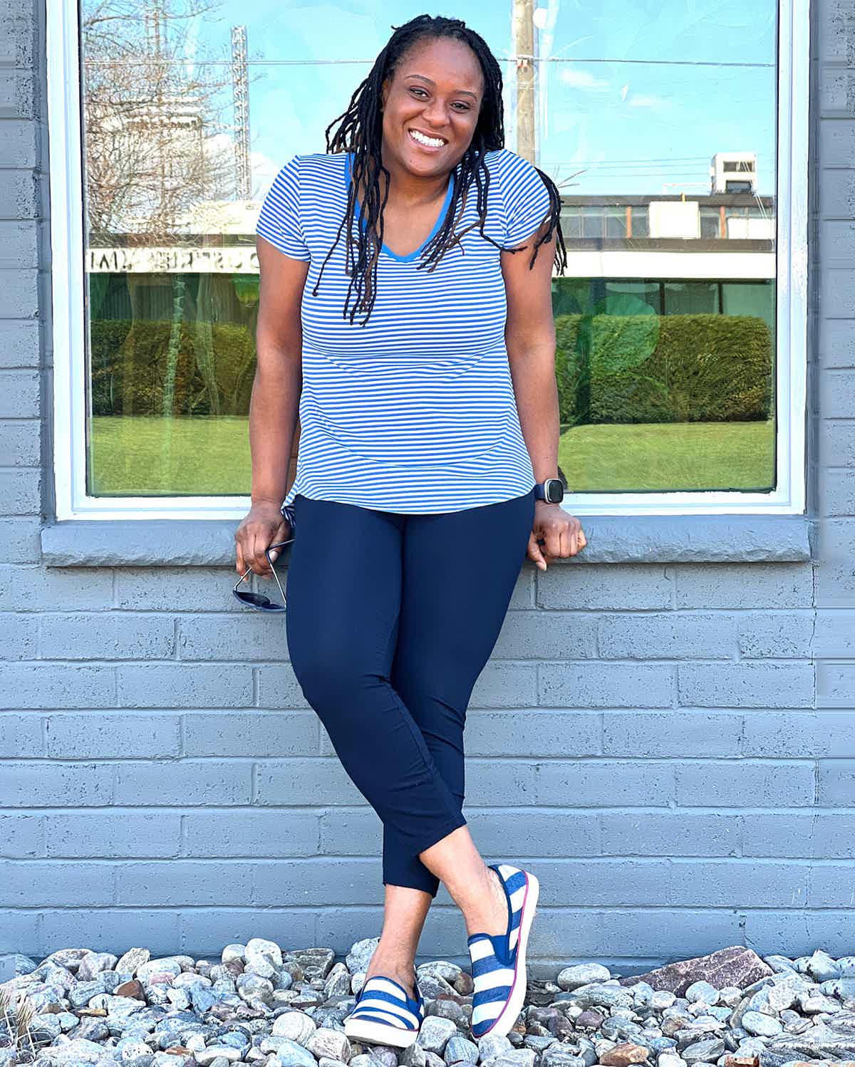 An image of a woman smiling in front of a window wearing Miik's Lisa2 capri legging in navy with striped blue t-shirt. 