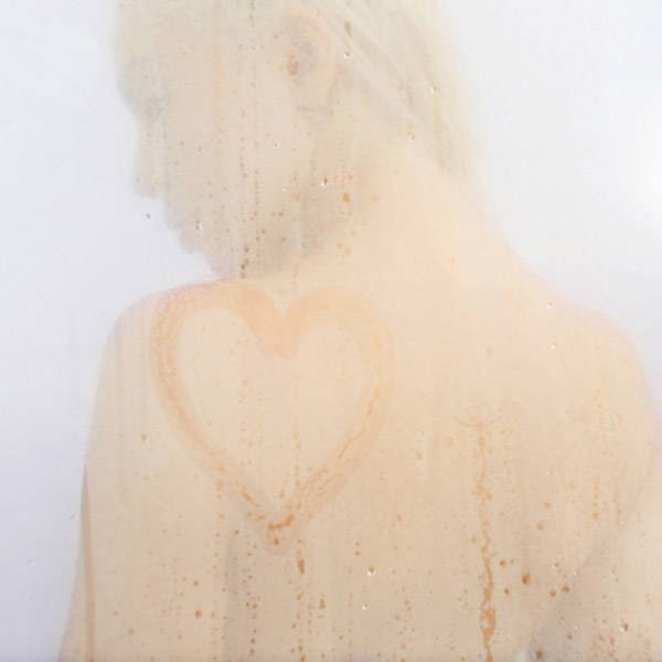 Femme derrière une porte de douche embuée avec un coeur peint dessus