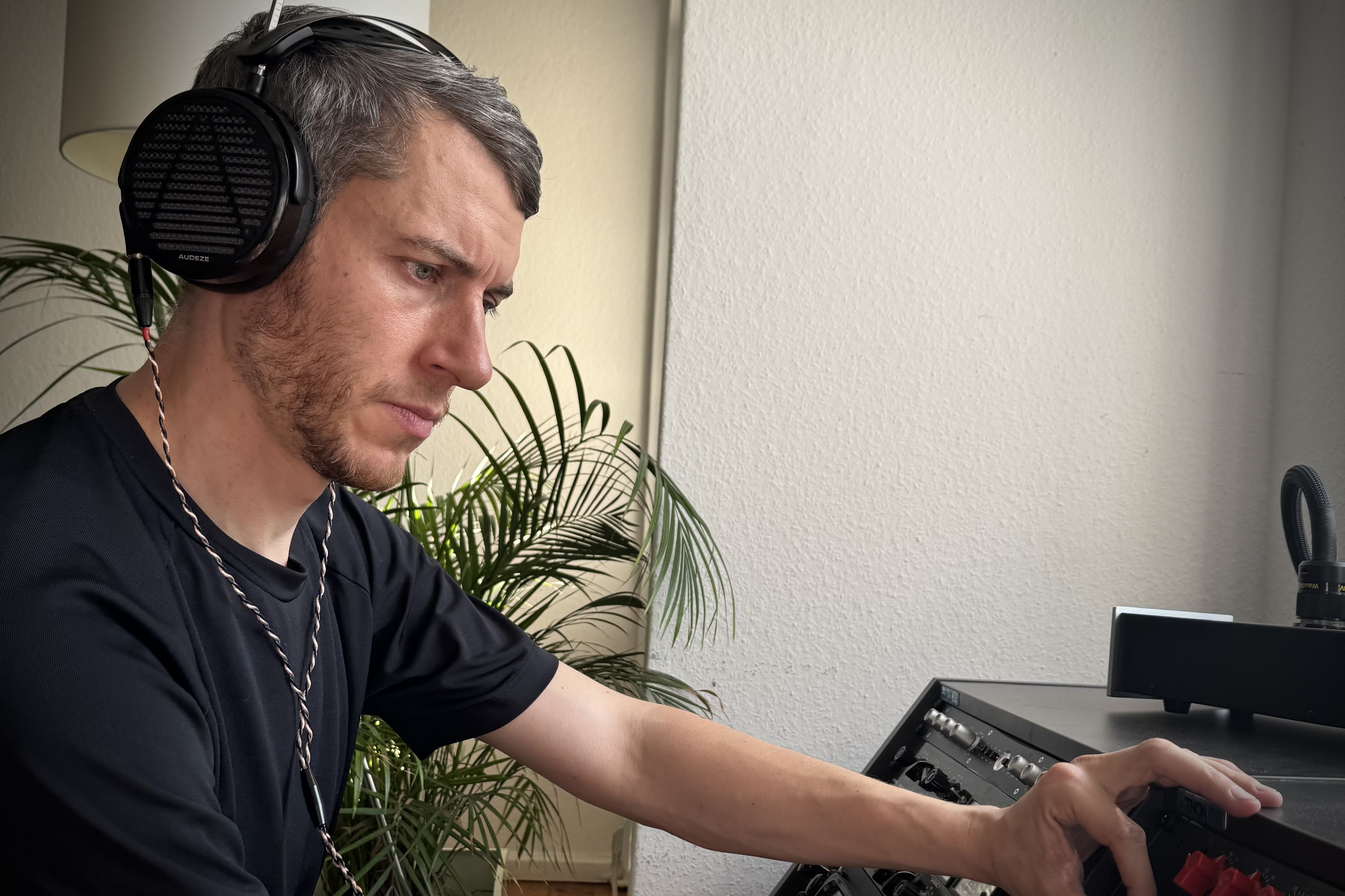 Conor Dalton wearing Audeze LCD-5 headphones, focused on a music setup with plants in the background.