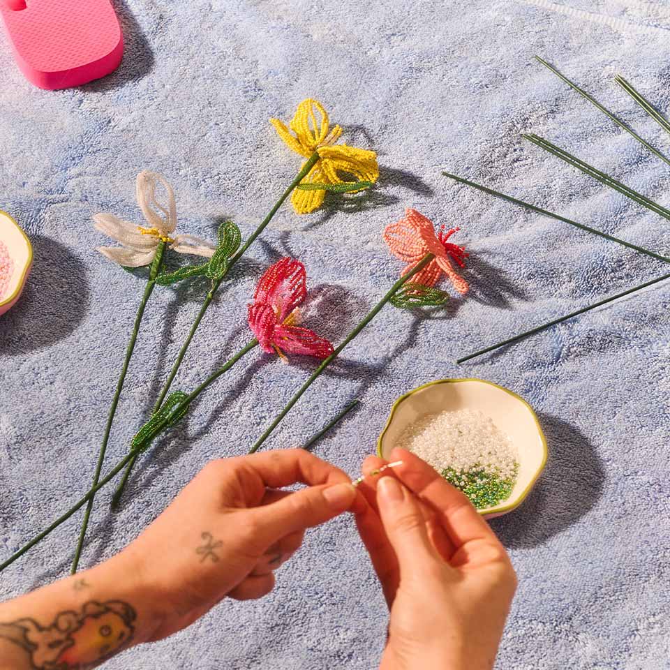 Hands arranging colorful flowers on a blue towel with a small bowl nearby.