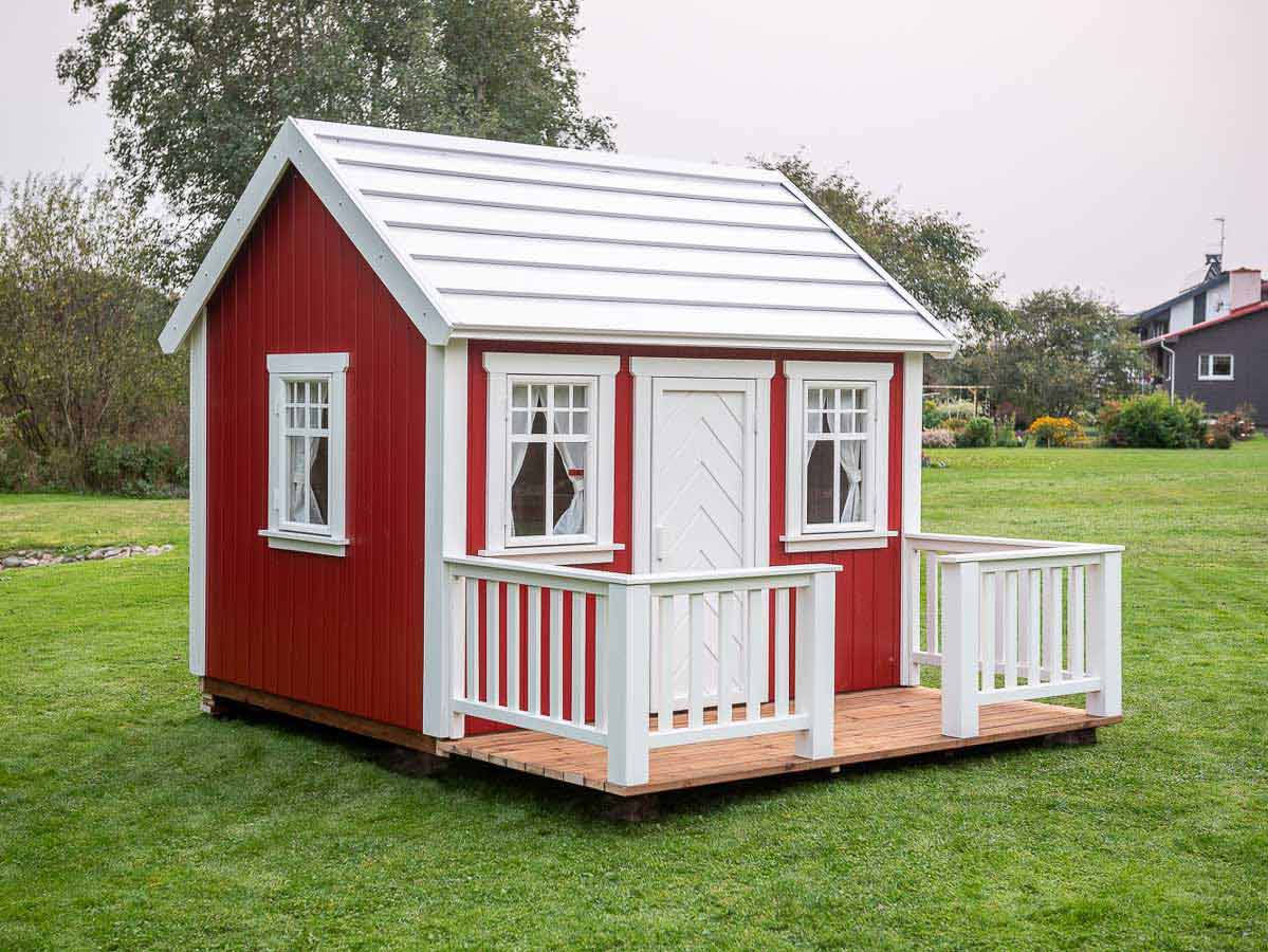 Red Outdoor Playhouse with white fishbone door, wooden terrace with white wooden railing on green lawn by WholeWoodPlayhouses
