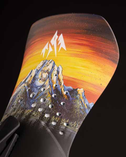 Snowboard tail with mountain and sunset graphic design.