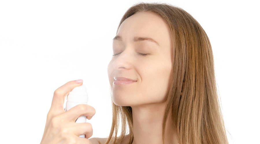 woman spraying her face with refreshing mist
