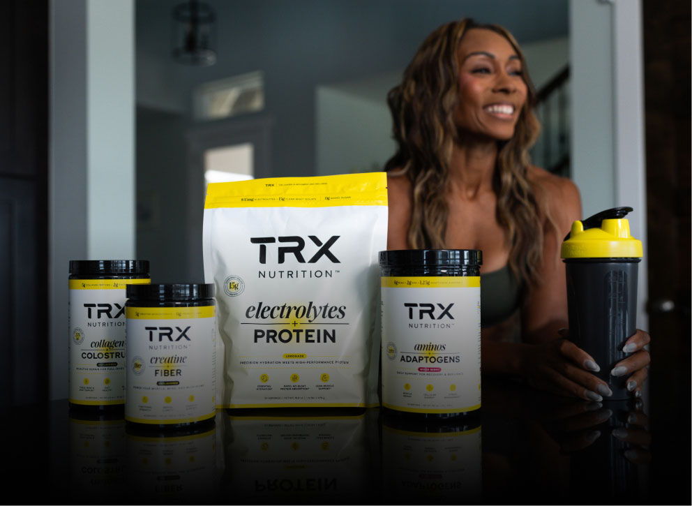 A woman smiling with TRX Nutrition products on a table.