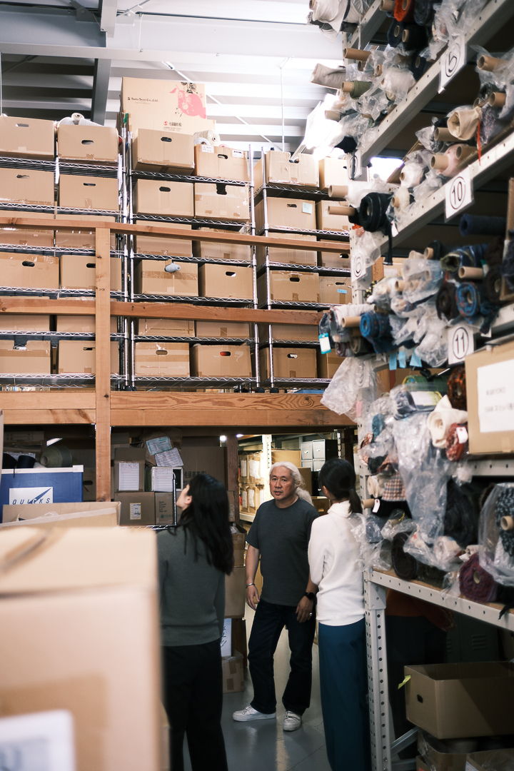 Two people standing in a storage area filled with boxes and materials.
