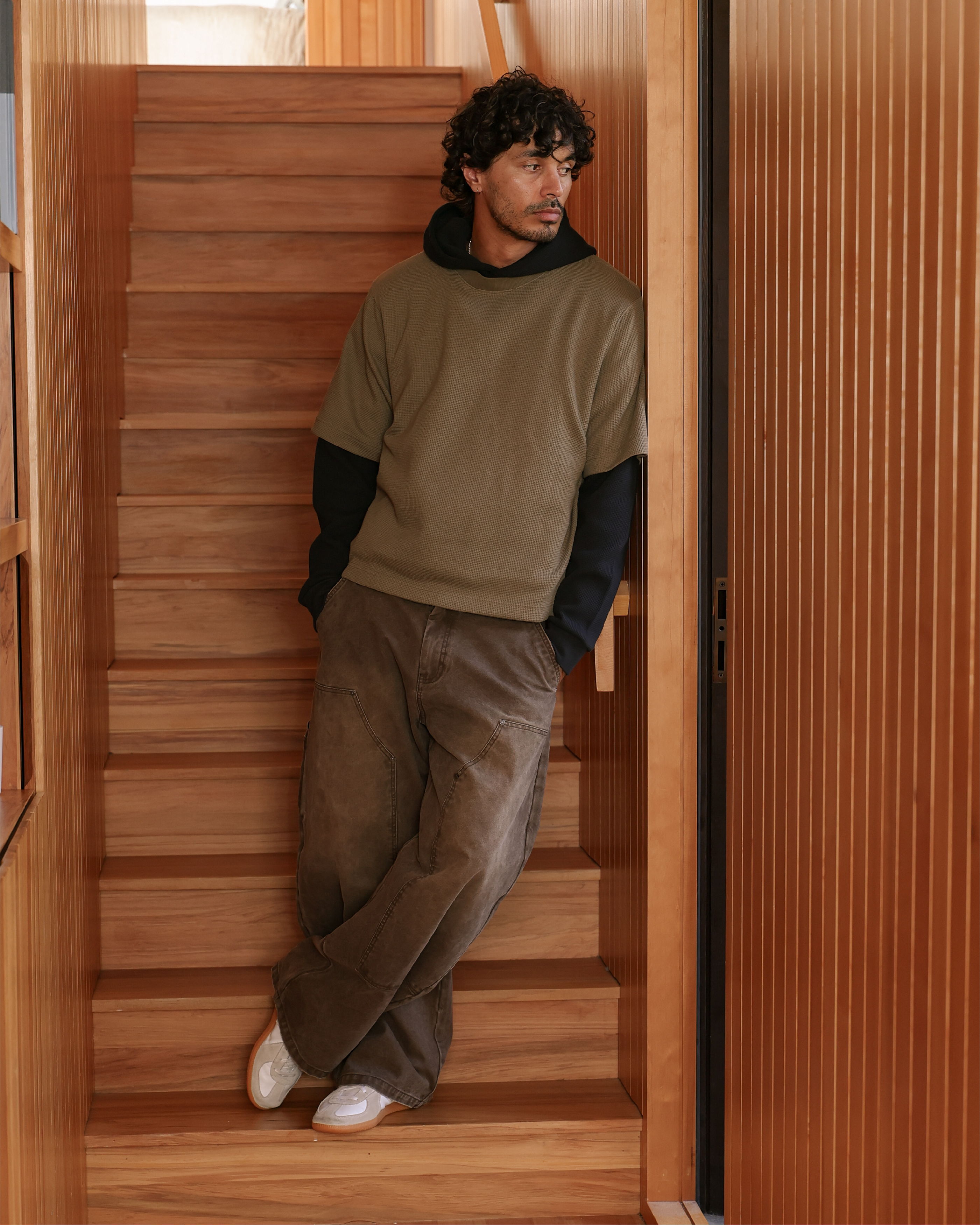 Person leaning against a wooden staircase, wearing casual clothing.