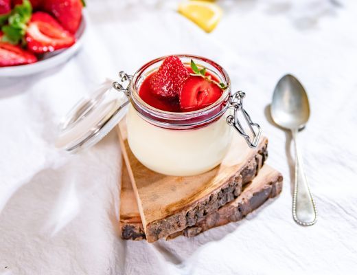 Dessert in a jar topped with strawberries on a wooden slice.