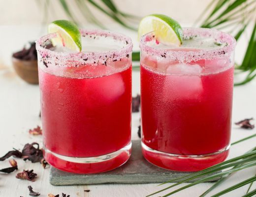 Two colorful cocktails with lime garnishes on a slate tray.