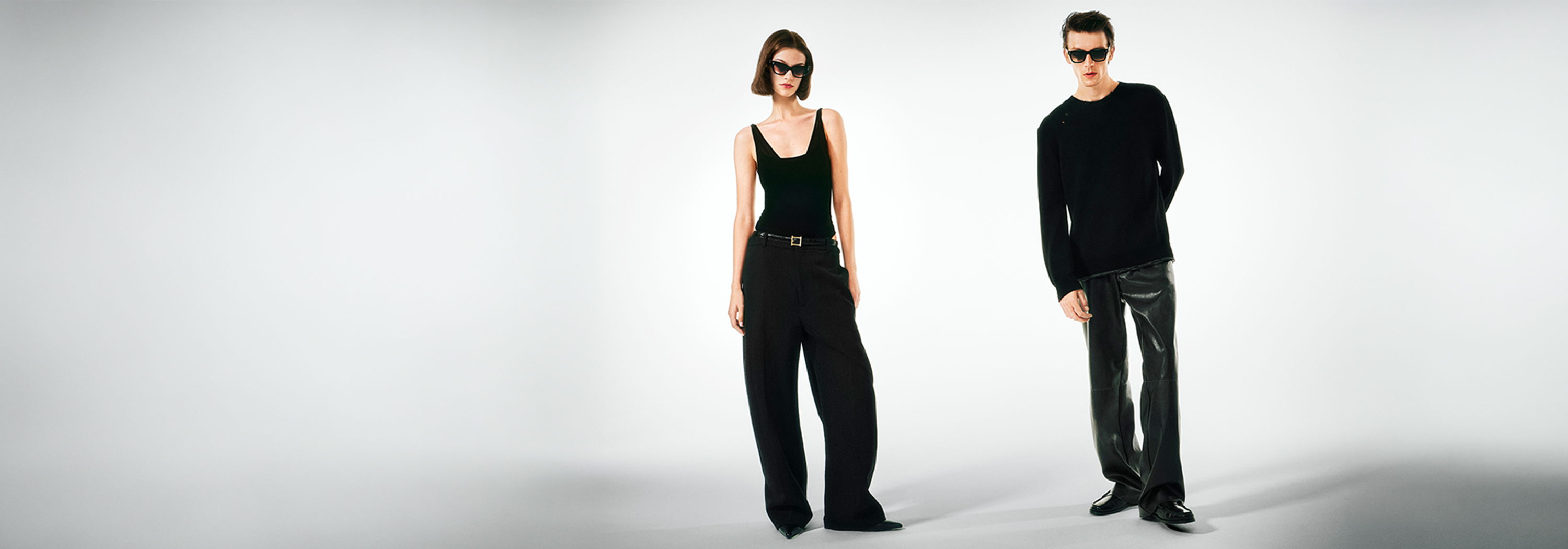 Two people in casual black clothing standing against a plain background.