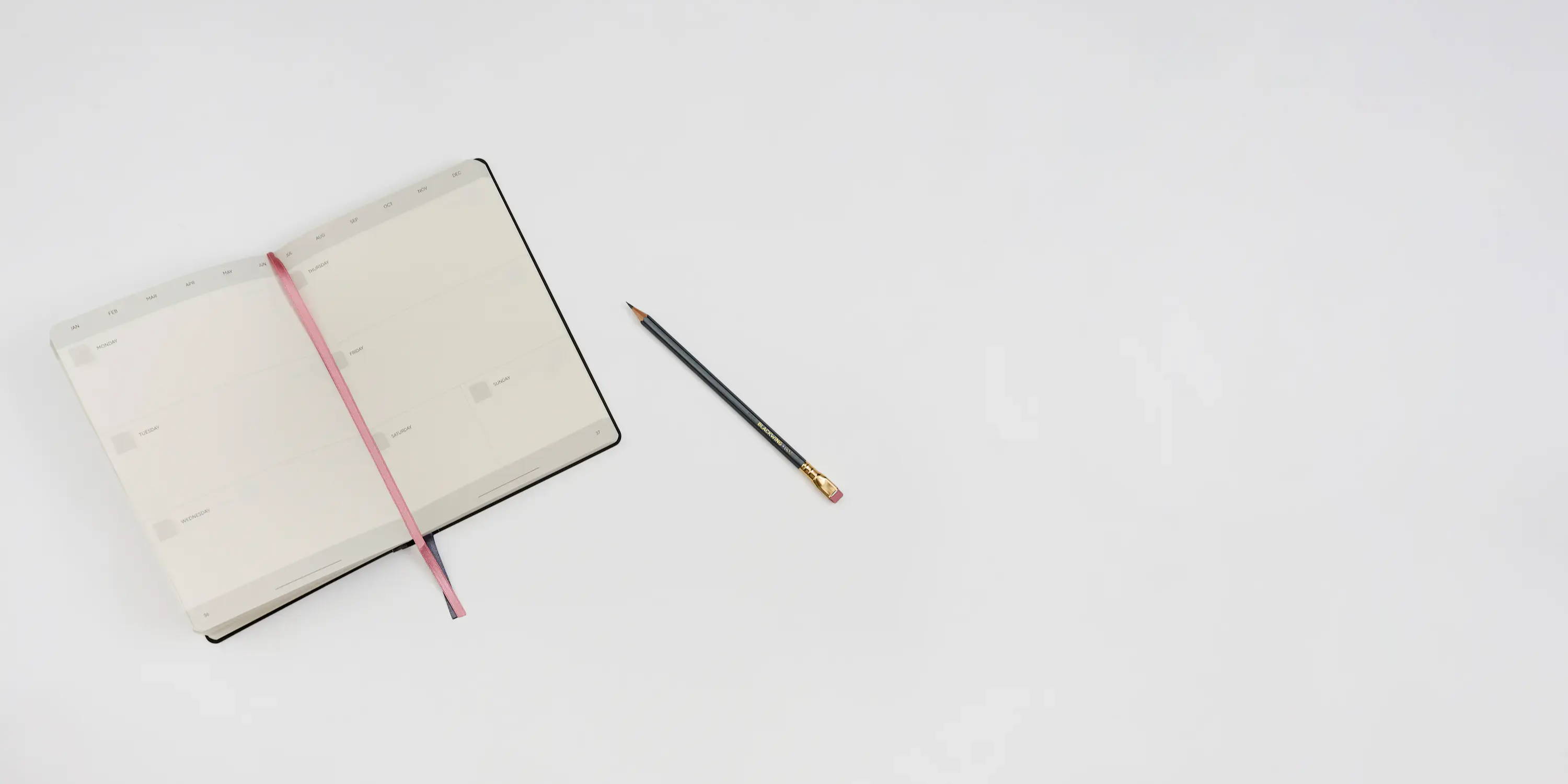 Open notebook with a red ribbon and a pencil on a white background.