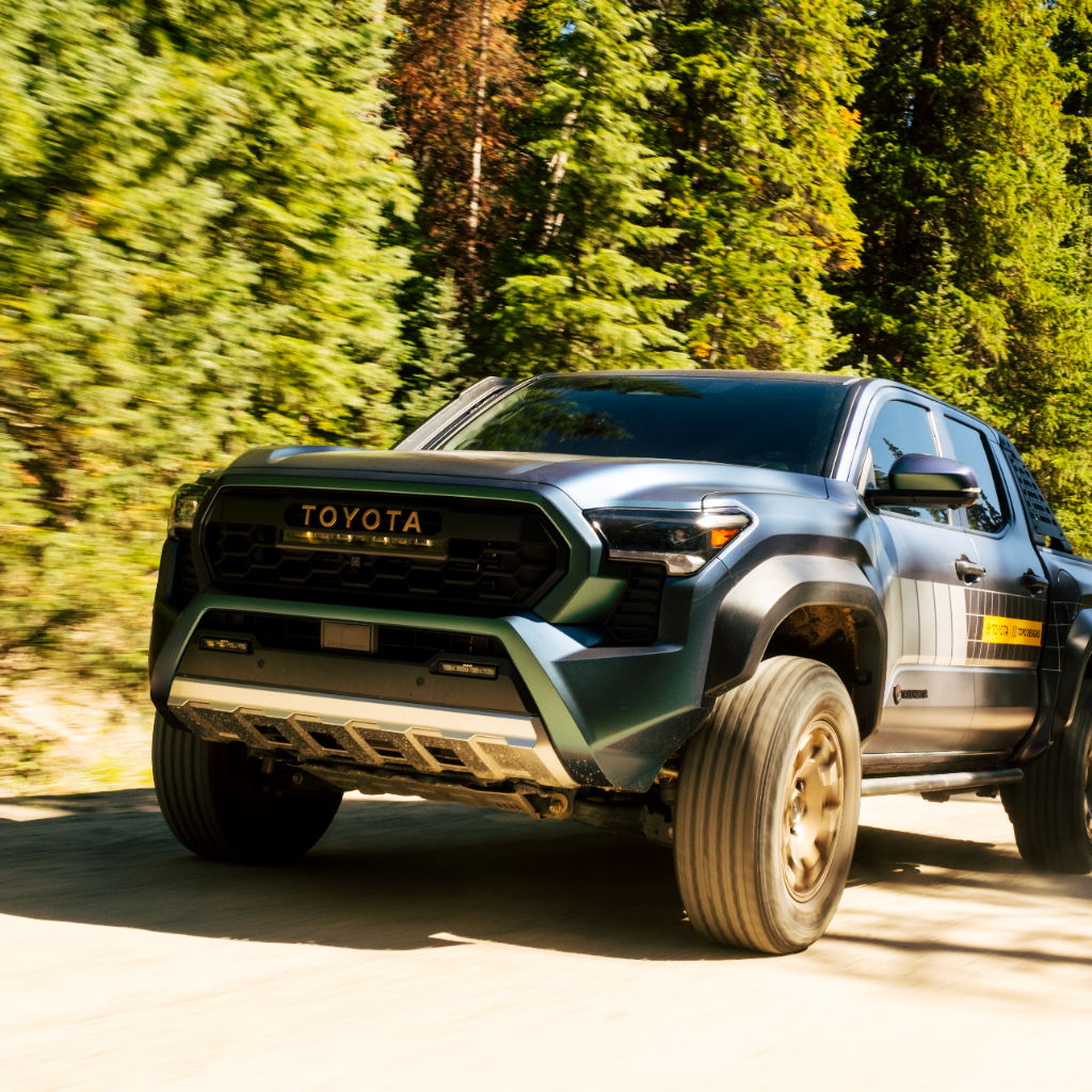 A blue Toyota truck driving on a dirt road surrounded by trees.