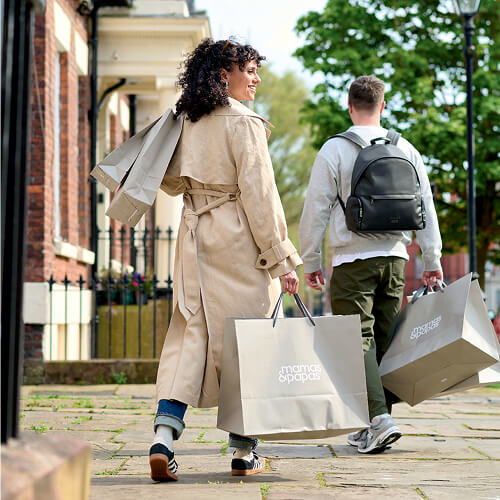 A woman and man carrying shopping bags on a sidewalk.