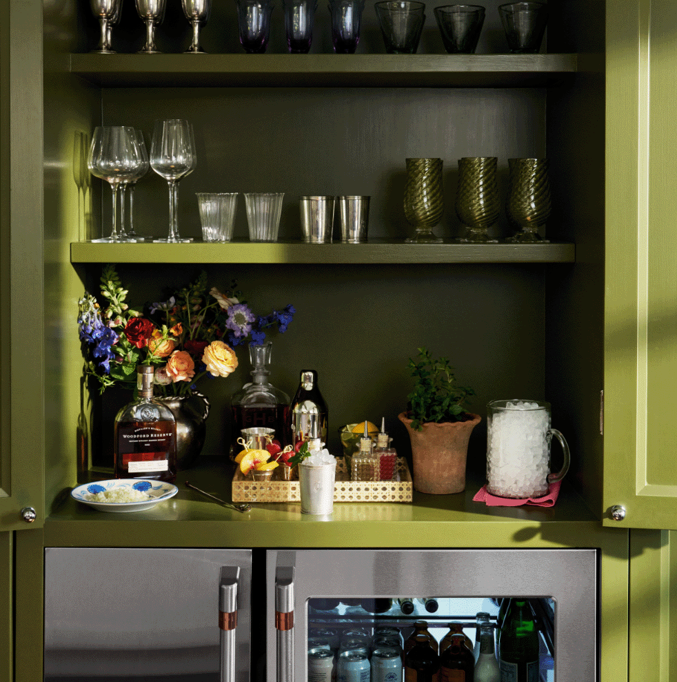 A stylish kitchen shelf with glasses, flowers, and a mini refrigerator.