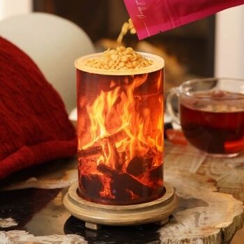 A container with a fire design, pouring contents, next to a cup of tea.