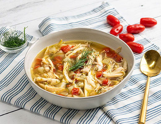 Bowl of soup with chicken, tomatoes, herbs, and a golden spoon.