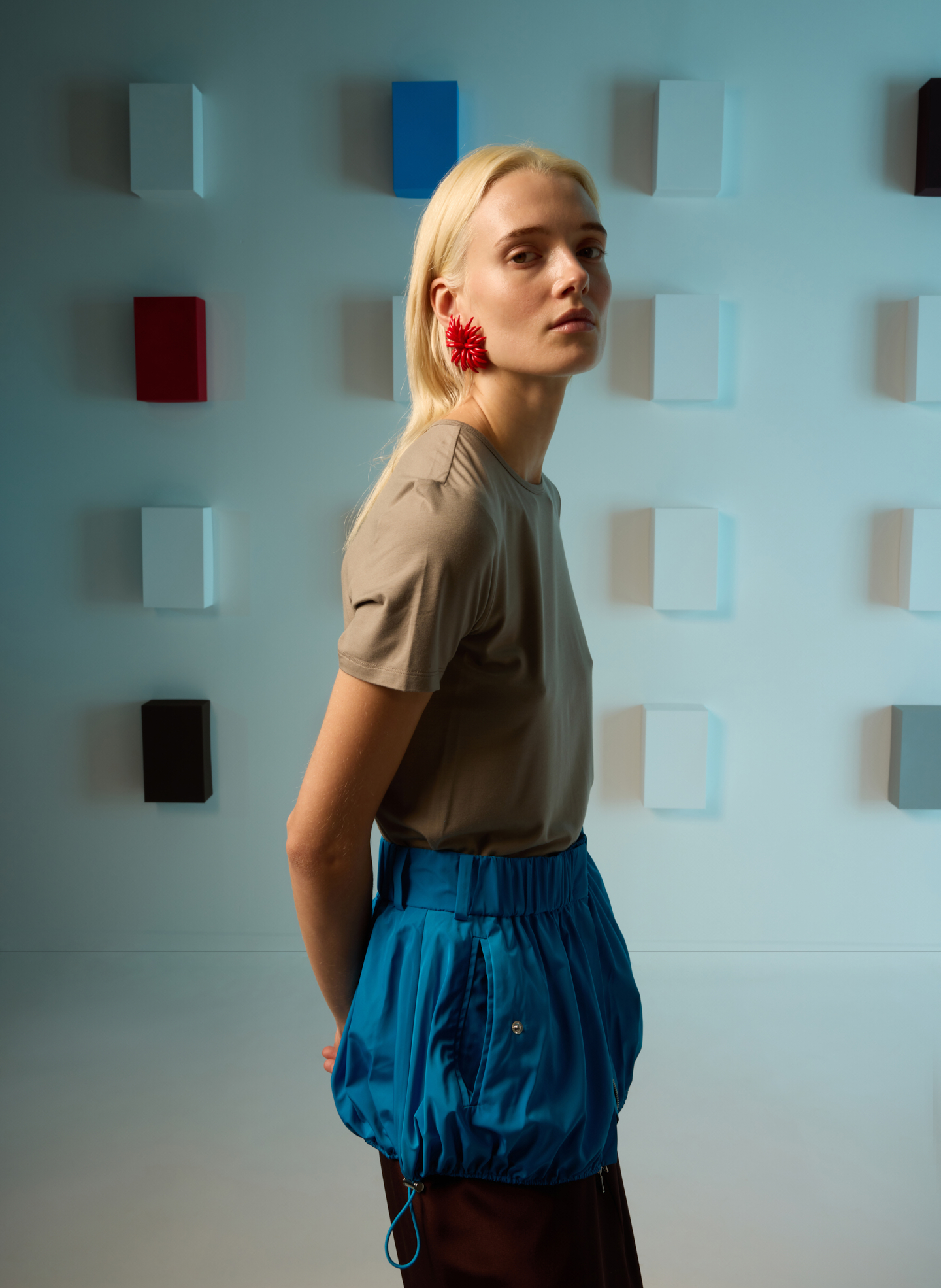 A model wearing a beige top and blue skirt against a colorful background.
