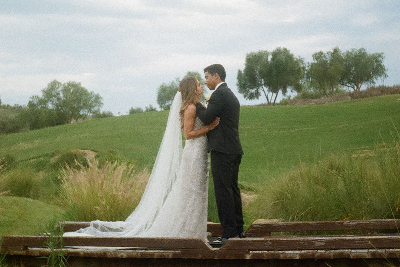 A bride and groom share a kiss outdoors on their wedding day.