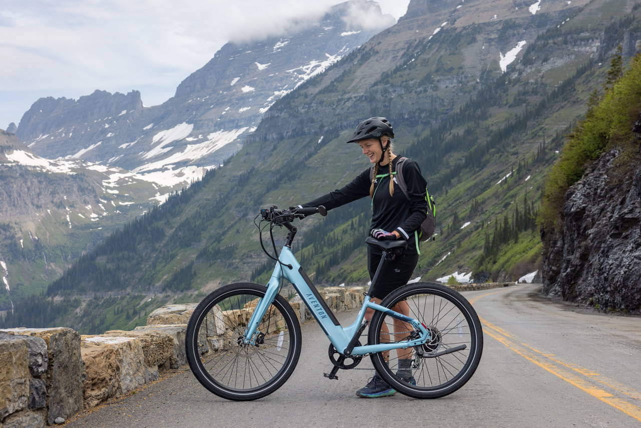 woman standing next to a blue Aventon electric bike with mountains in the background