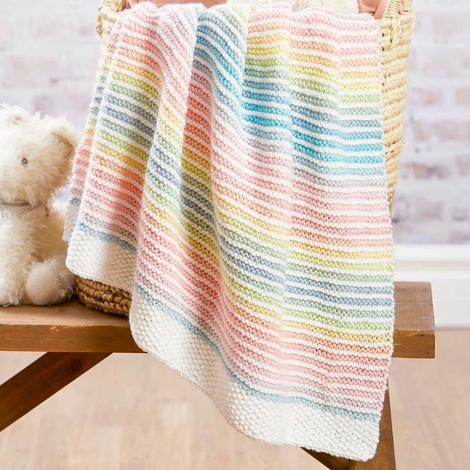 Colorful striped blanket draped over a basket beside a teddy bear.