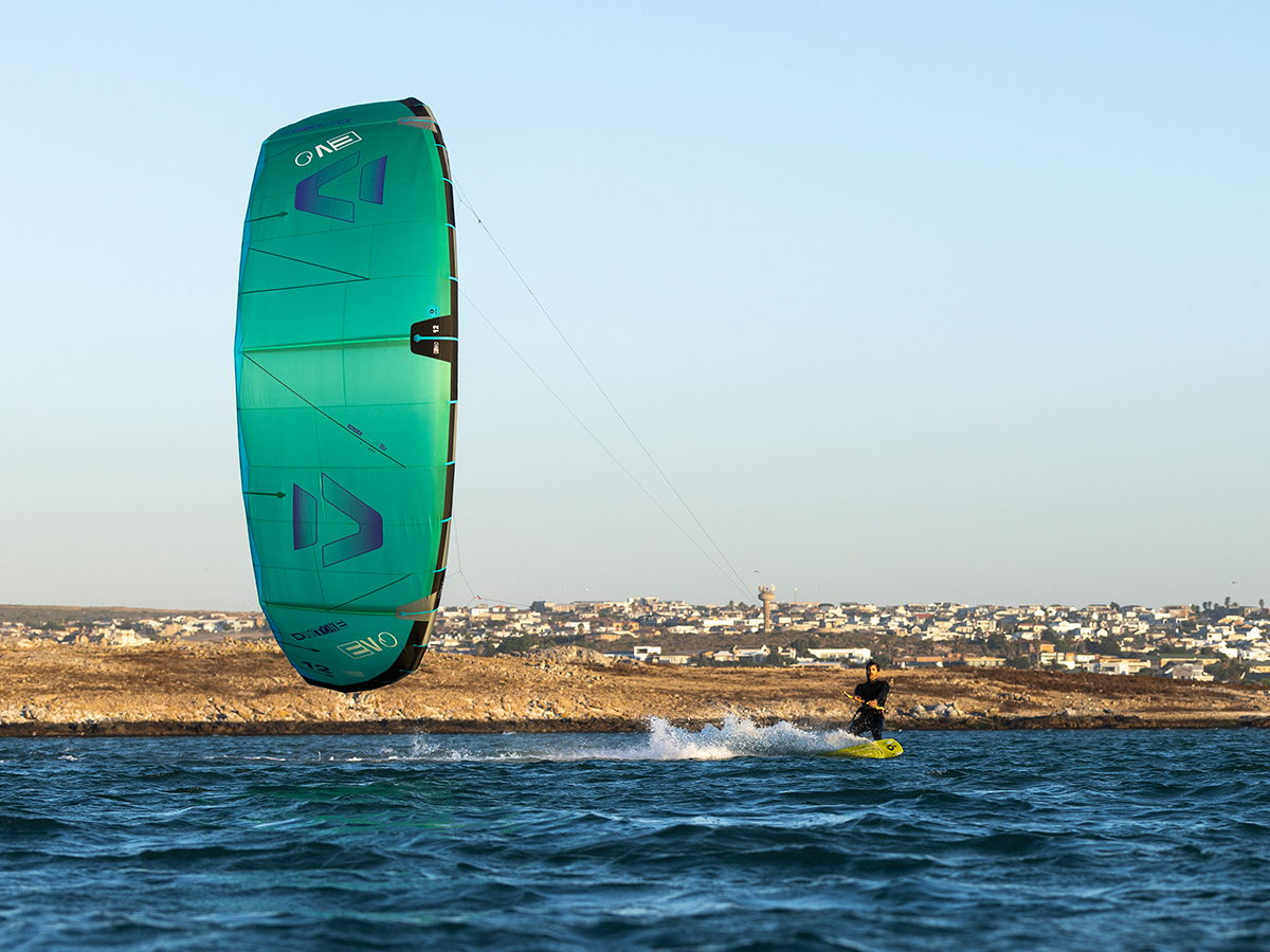 A person kitesurfing with a green kite over water.