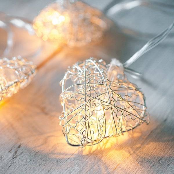 Silver heart fairy lights with a warm white bulb on a wooden surface.