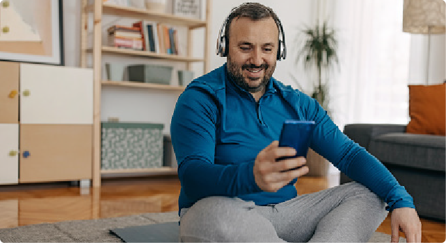 Man sitting on the floor, smiling while using a smartphone and wearing headphones.