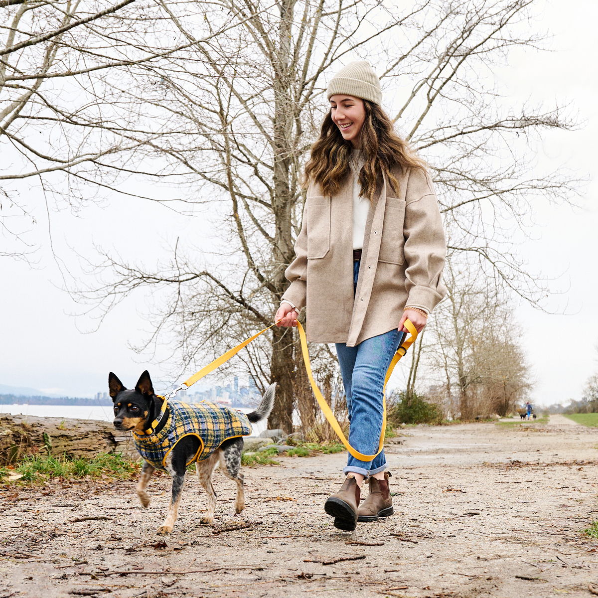 Woman walking a dog on a path surrounded by trees.