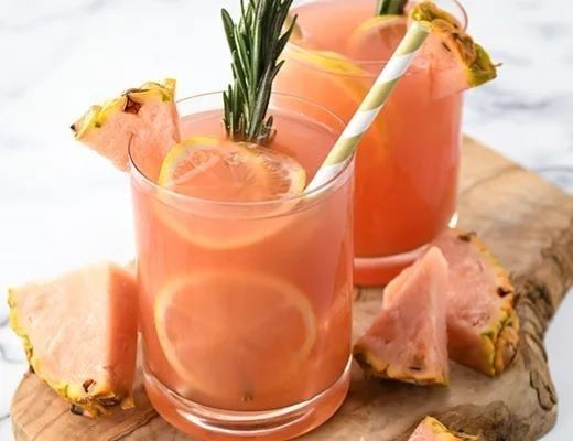 Two glasses of pink drinks with lemon, garnished with rosemary and pineapple.