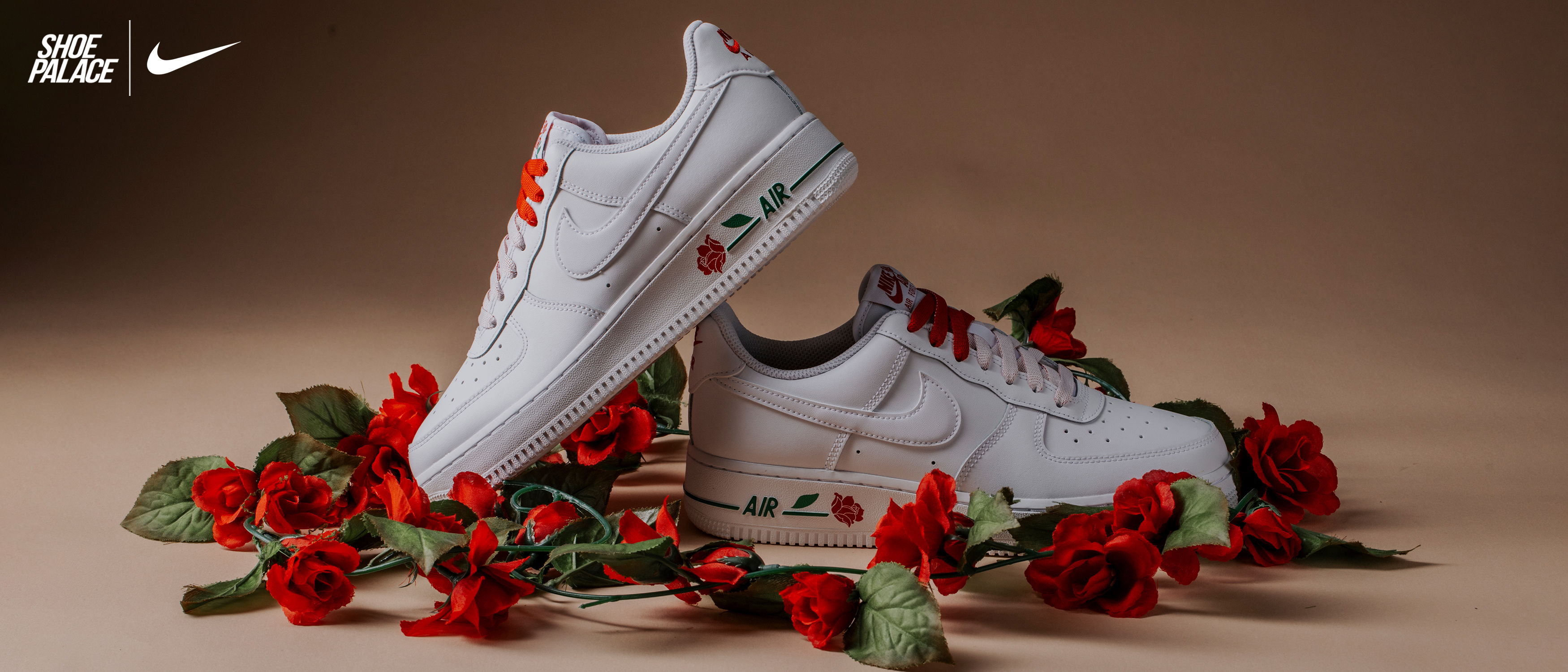White Nike sneakers surrounded by red roses on a neutral background.