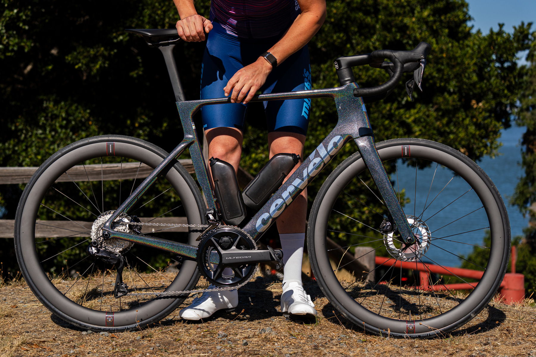 A cyclist stands next to a sleek, modern bicycle on a scenic path.