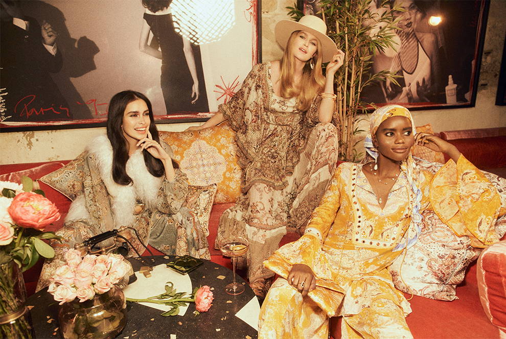 Models wearing CAMILLA paisley, floral layered outfits in bar with cocktails