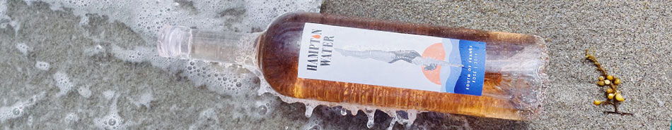 A bottle in shallow water with waves splashing around it.