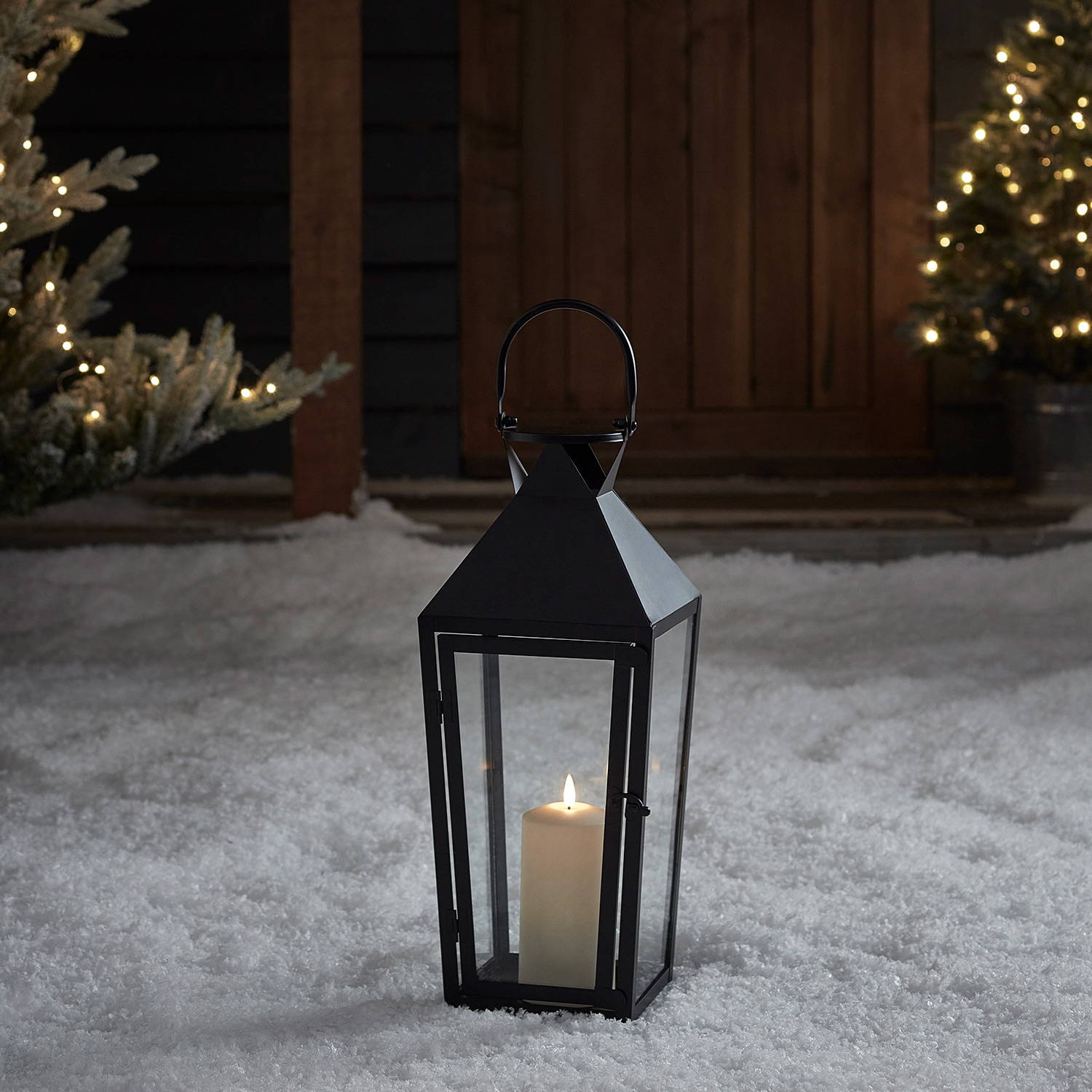A black metal outdoor lantern with LED candle within in a snowy setting