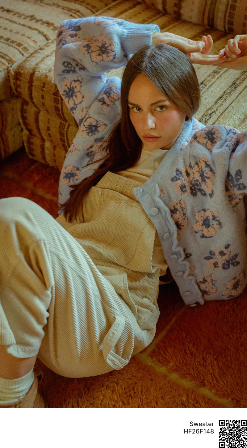 Young woman in floral sweater and overalls, lounging on a patterned couch.