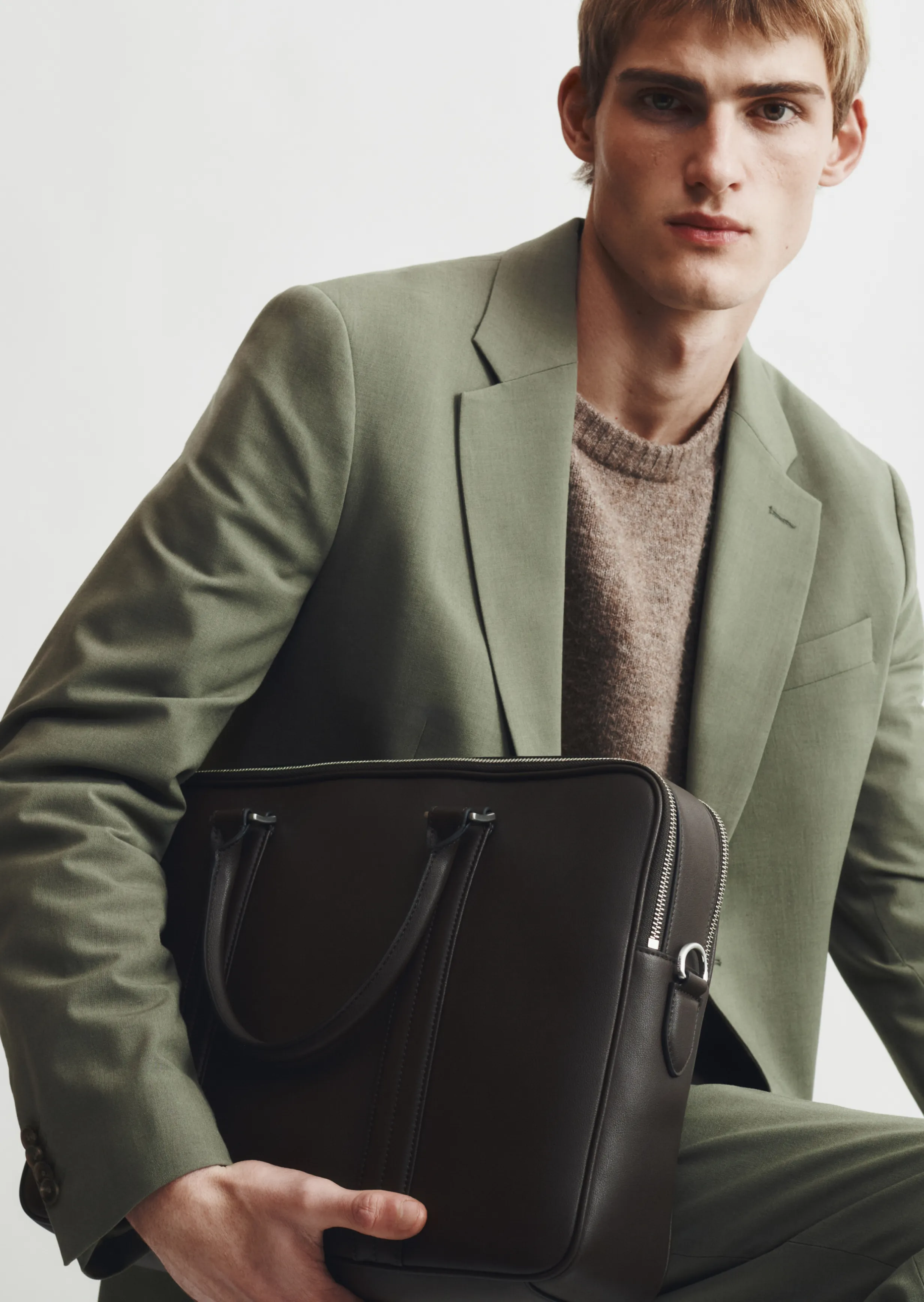 Young man in a green suit holding a dark bag.