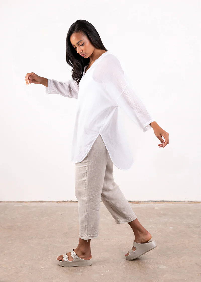 A model wearing a semi sheer white cotton oversized shirt with off white trousers and off white chunky platform slides
