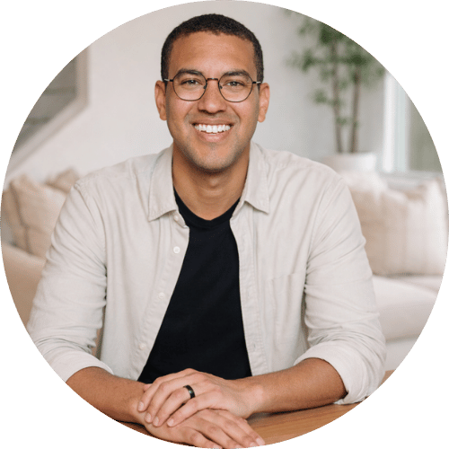 Smiling man wearing glasses, sitting at a table in a bright room.