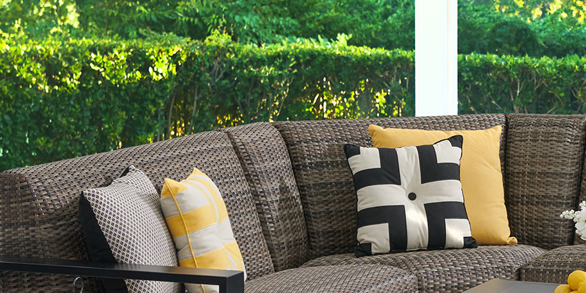 Outdoor seating area with decorative pillows and greenery in the background.
