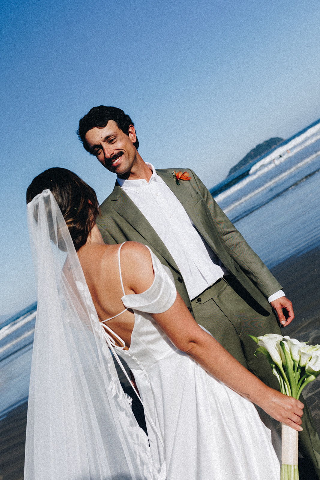 A bride and groom smiling at each other on the beach.