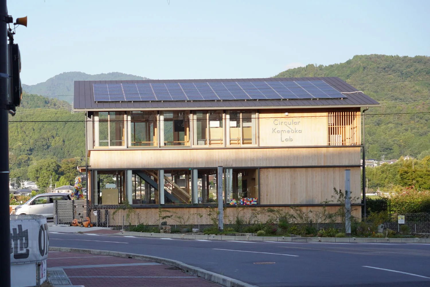 A modern building with solar panels near a road and mountains.