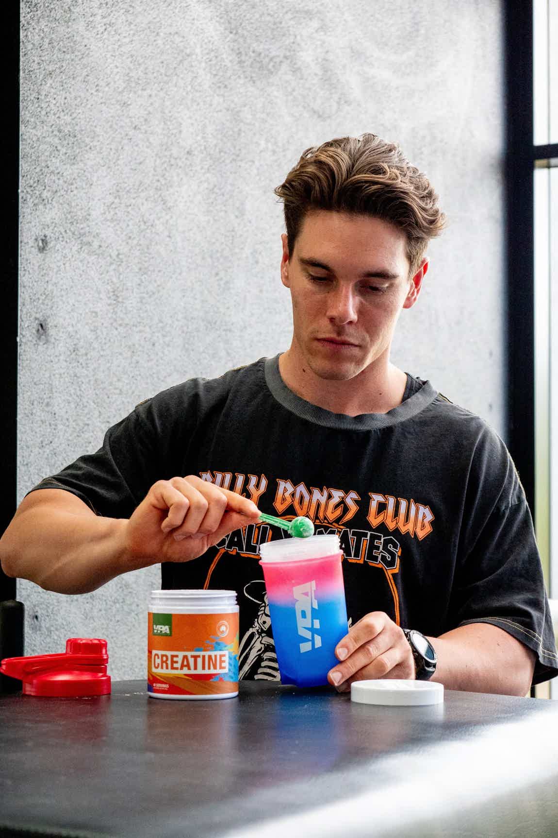 Man mixing creatine powder in a blue shaker bottle at a table.